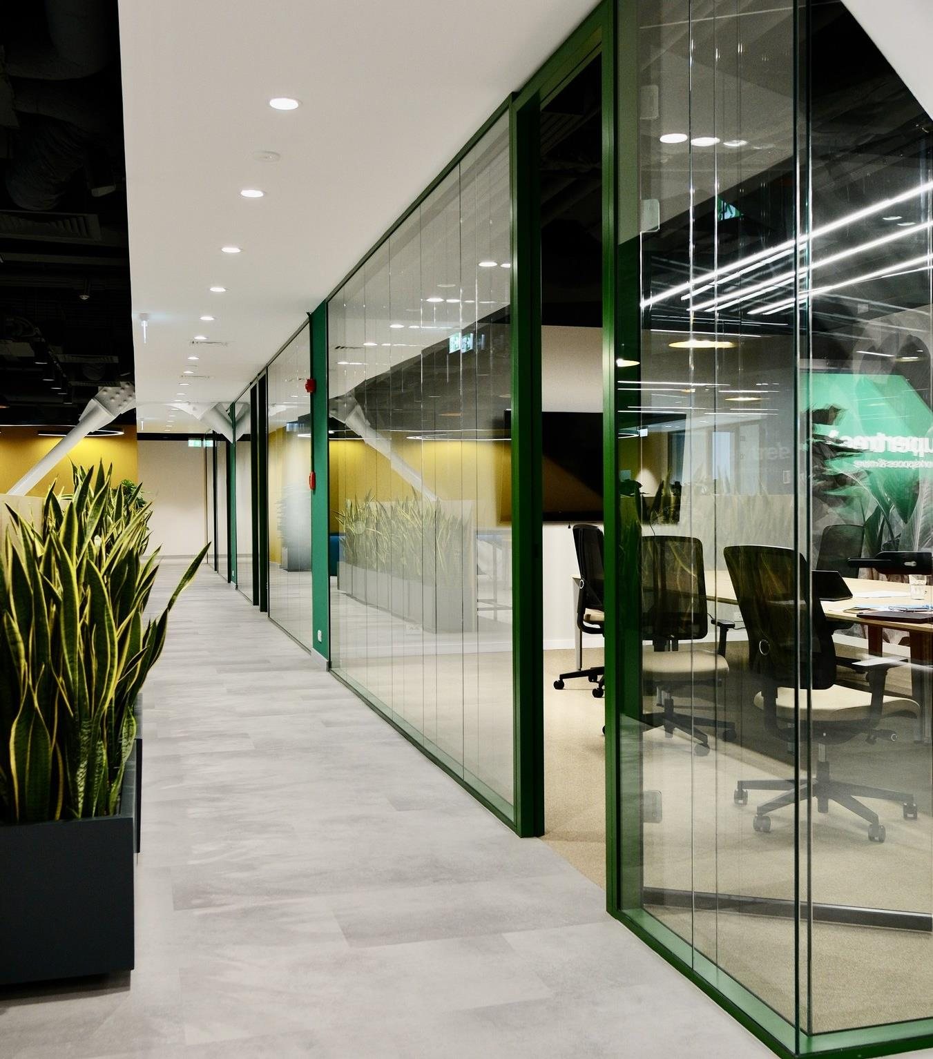 Glass-fronted offices with green frames along a corridor at Supertree, BOC Tower